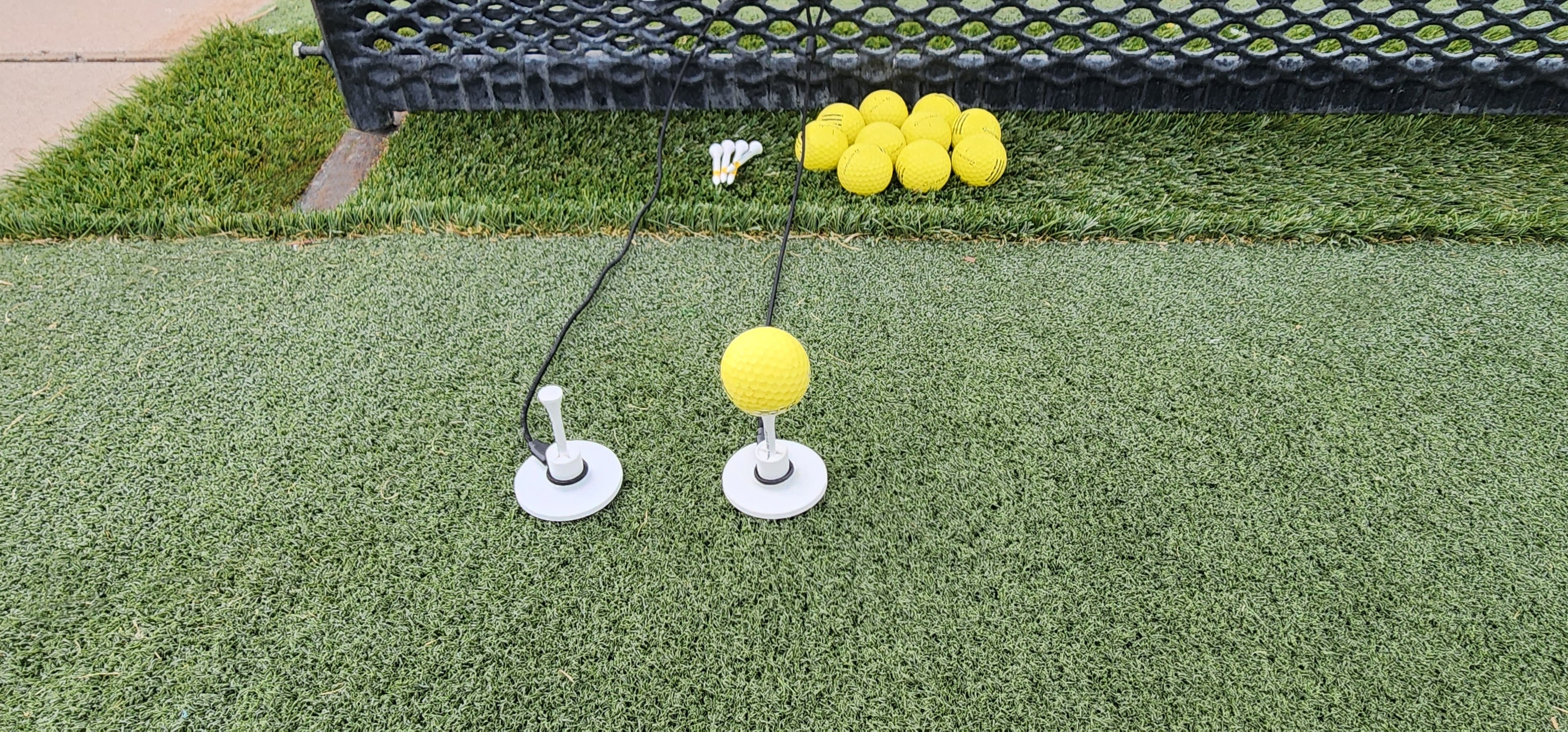 Tee Leashes — blog image — range setup with two Tee Leashes and one range ball on wood tee in rubber tee with durable elastic cords attached to range basket on turf