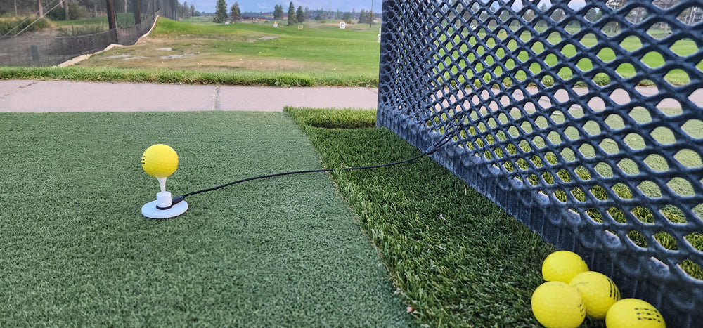 Tee Leash TL-O1 Original — product image — range setup with rubber tee tethered and attached to range fence with range balls on turf